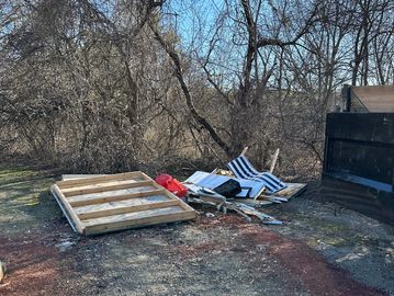 Discarded wooden frame and debris near a dumpster on a sunny day.