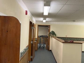 Office hallway with carpet, wooden doors, and a ladder at the end.