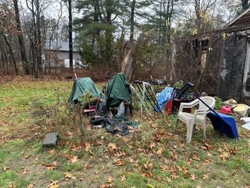 Backyard clutter with covered lawn mowers, chairs, and gardening tools.
