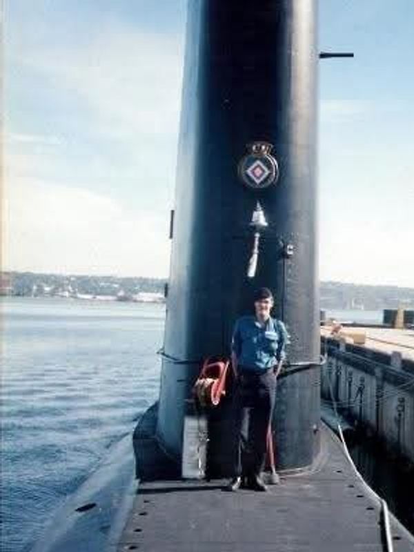 Man standing on a submarine near dock.