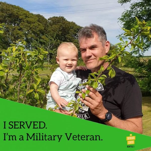 Military veteran holding a baby in a garden.