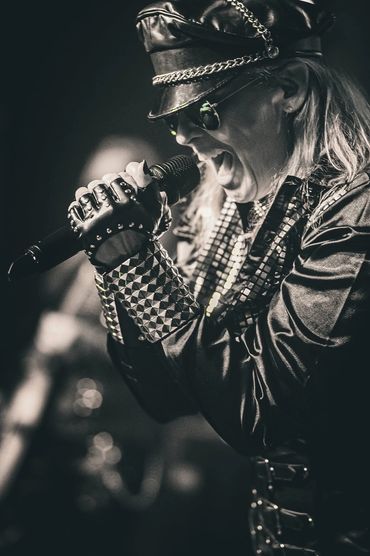 Rock singer passionately performing in studded leather outfit and cap.