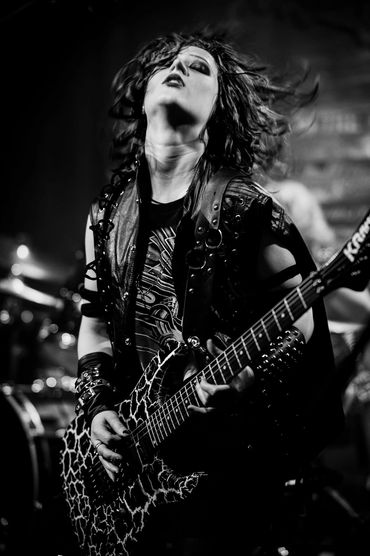 Energetic guitarist passionately playing on stage with wild hair and leather outfit.