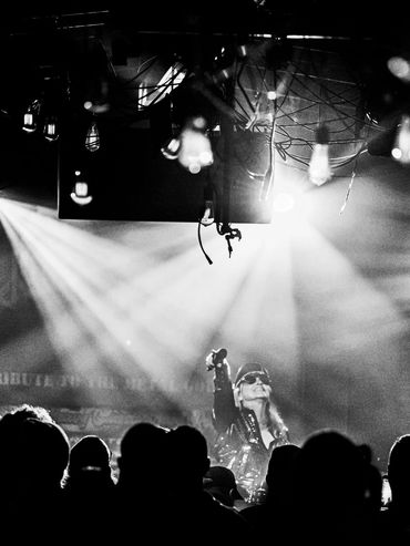 Black and white photo of a singer performing on stage with dramatic lighting and a crowd silhouette.
