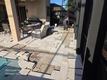 Workers restoring a patio with partially laid pavers near a pool.