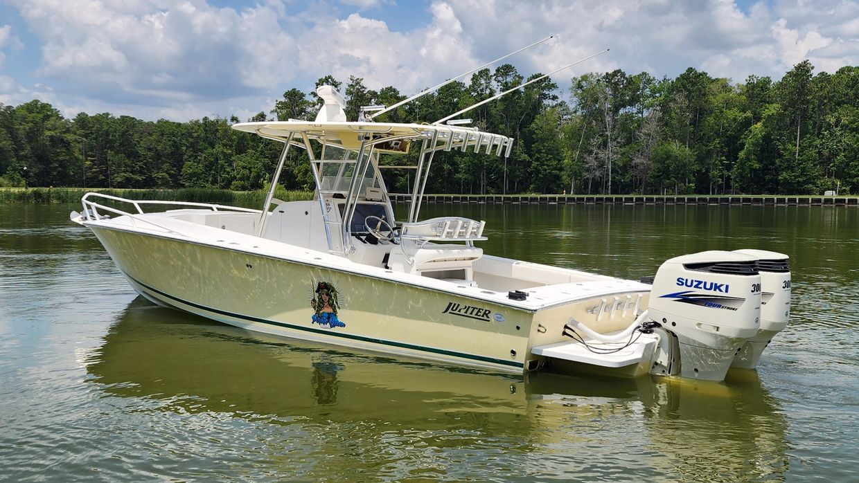 A sleek white fishing boat on calm water near a forested shore.