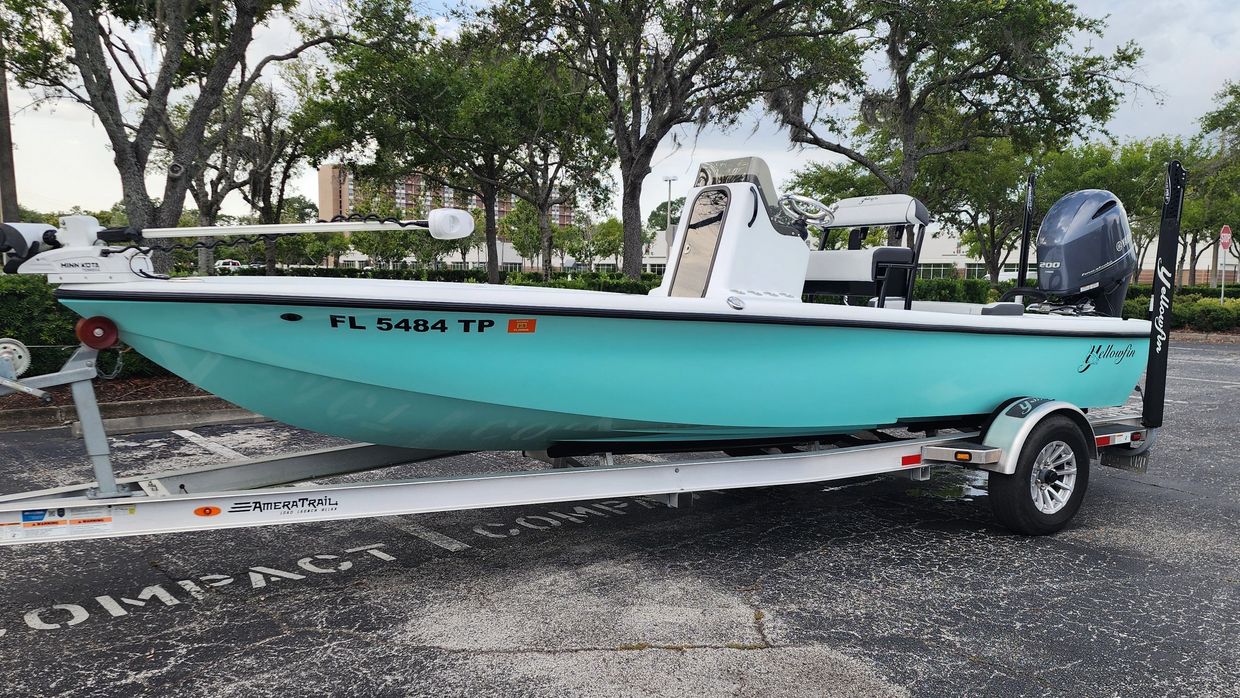 Light blue fishing boat on a trailer in a parking lot.