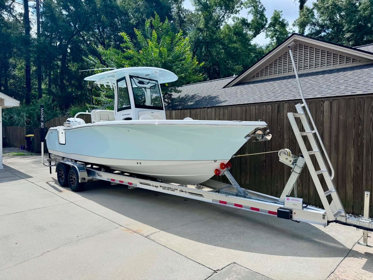 White boat on a trailer parked by a wooden fence.