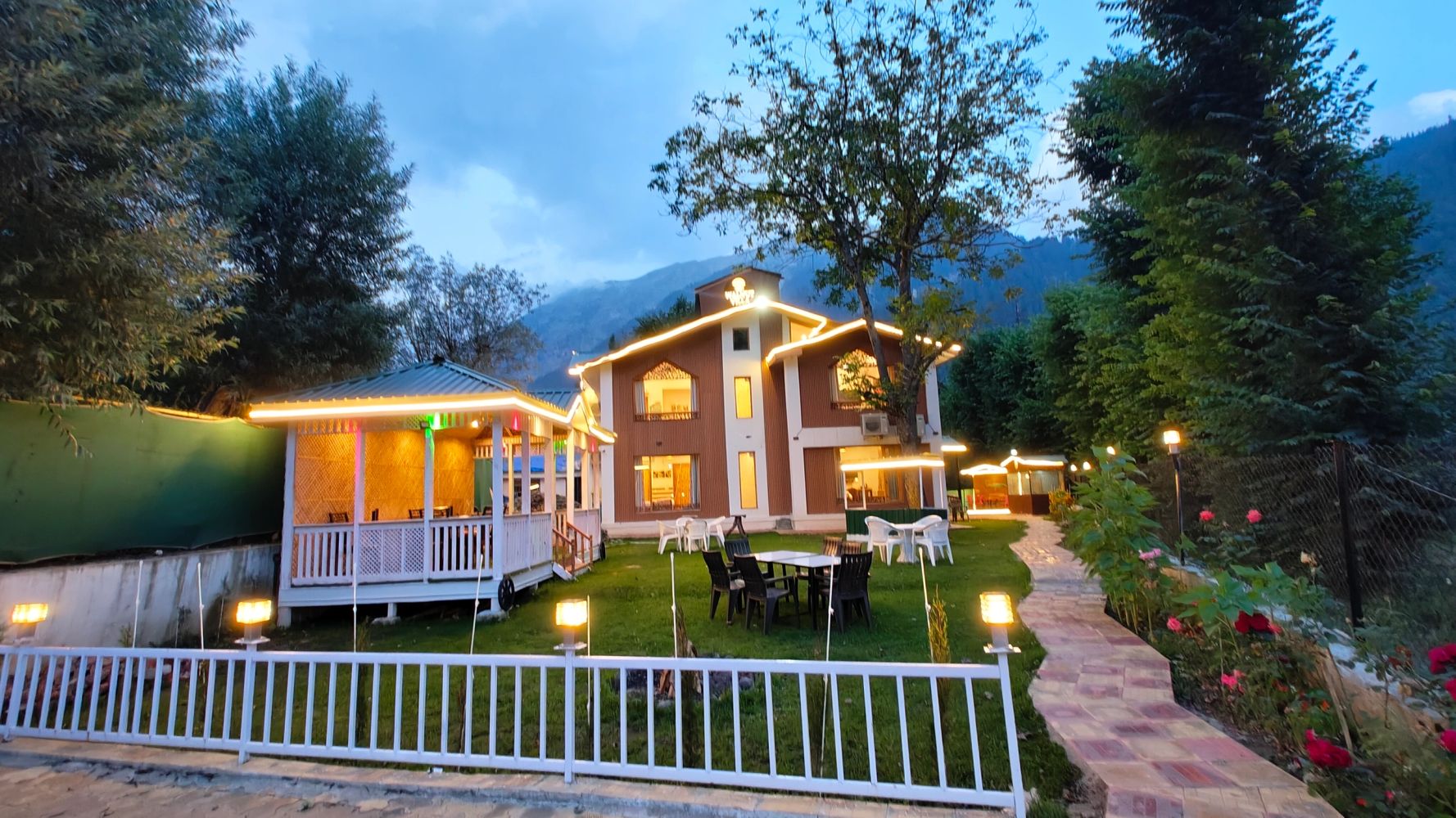 A warmly lit house with outdoor seating and garden at dusk.
