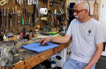 Robert Champion sitting at workbench holding a knife