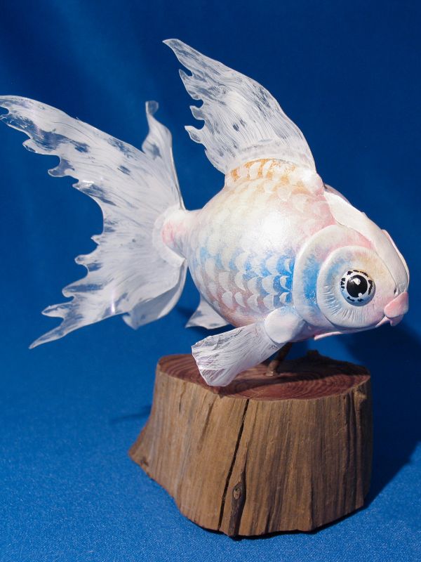 A delicate white fish sculpture with translucent fins on a wooden base.