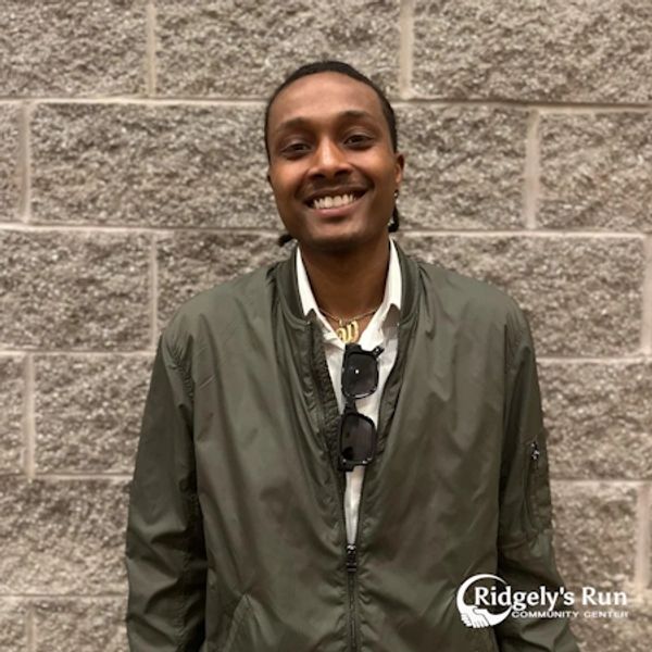Smiling man in green jacket standing against stone wall.