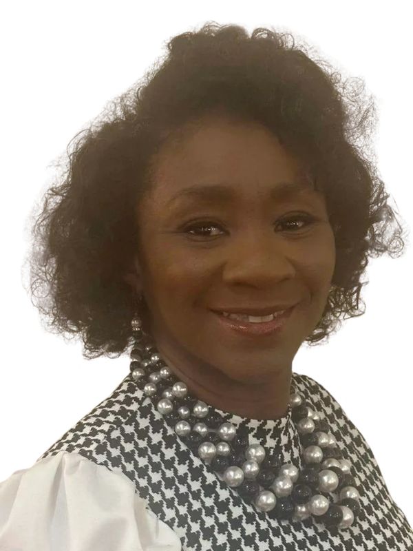 A woman with curly hair wearing a pearl necklace and patterned top smiles.