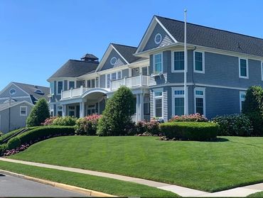 Large blue-gray house with manicured lawn and bushes under clear sky.