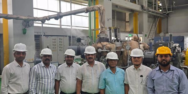 Seven men in safety helmets stand inside an industrial facility.