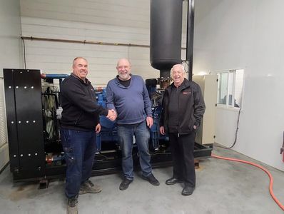Three men shake hands and smile in an industrial room with equipment.