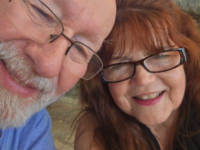 Close-up selfie of a smiling elderly couple wearing glasses.