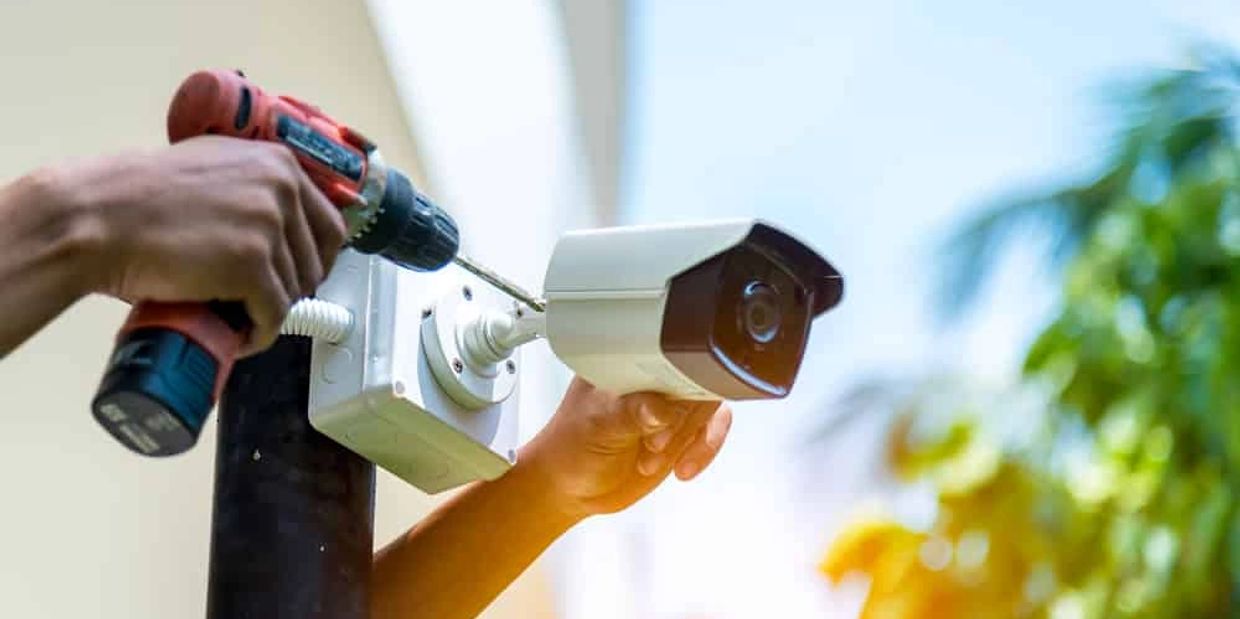 Person installing a security camera with a drill.