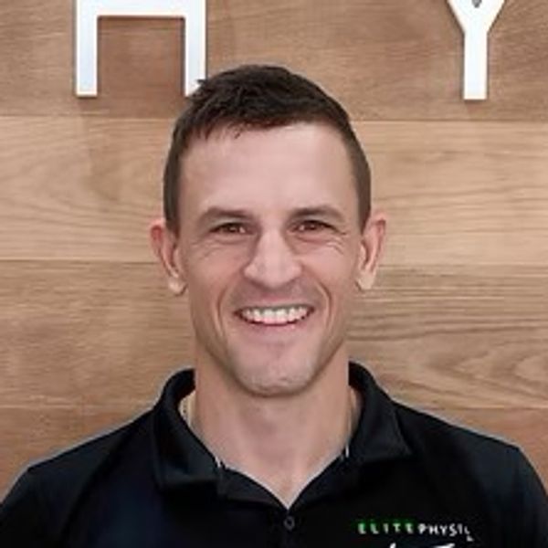 Smiling man in a black shirt against a wooden background.