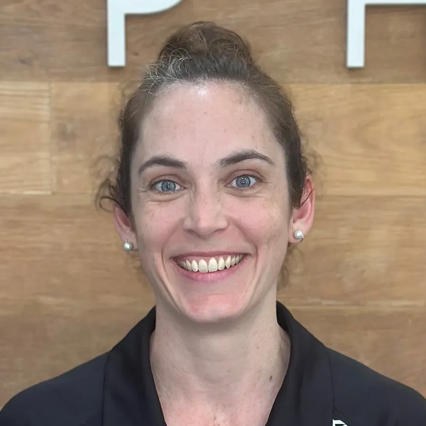 Smiling woman with blue eyes and pearl earrings.