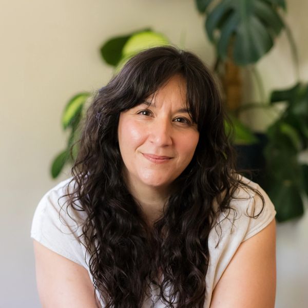 Smiling woman with long dark curly hair in a white shirt.