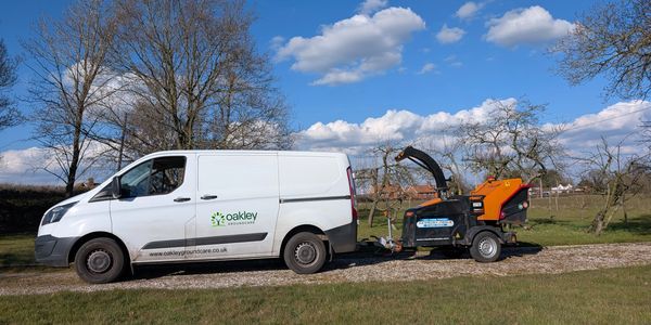 White Oakley Groundcare van towing a wood chipper on a sunny day.