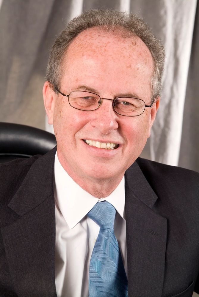Grant's headshot, glasses, white shirt, blue tie, dark grey suit jacket