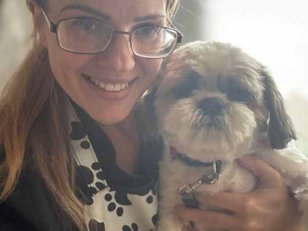 Woman with glasses smiling while holding a small dog.