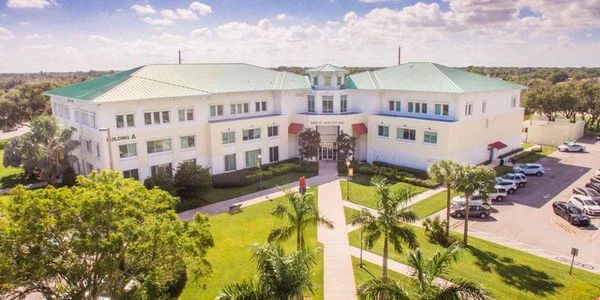 Port Saint Lucie City Hall. A large white building with green roofs and palm trees under a partly cloudy sky.