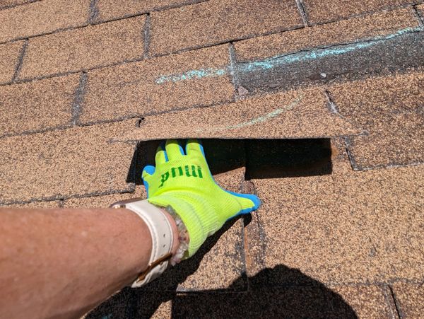 Person wearing a glove lifts a roof shingle.