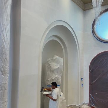 Painter applying plaster to a wall with arched architectural details.