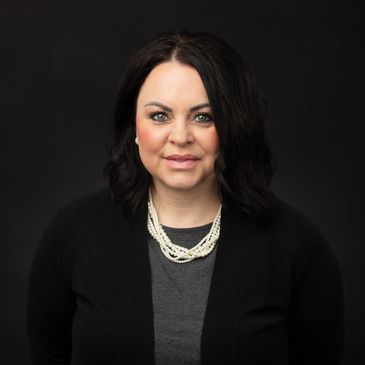Professional portrait of a woman with dark hair, wearing a black sweater and pearl necklace.