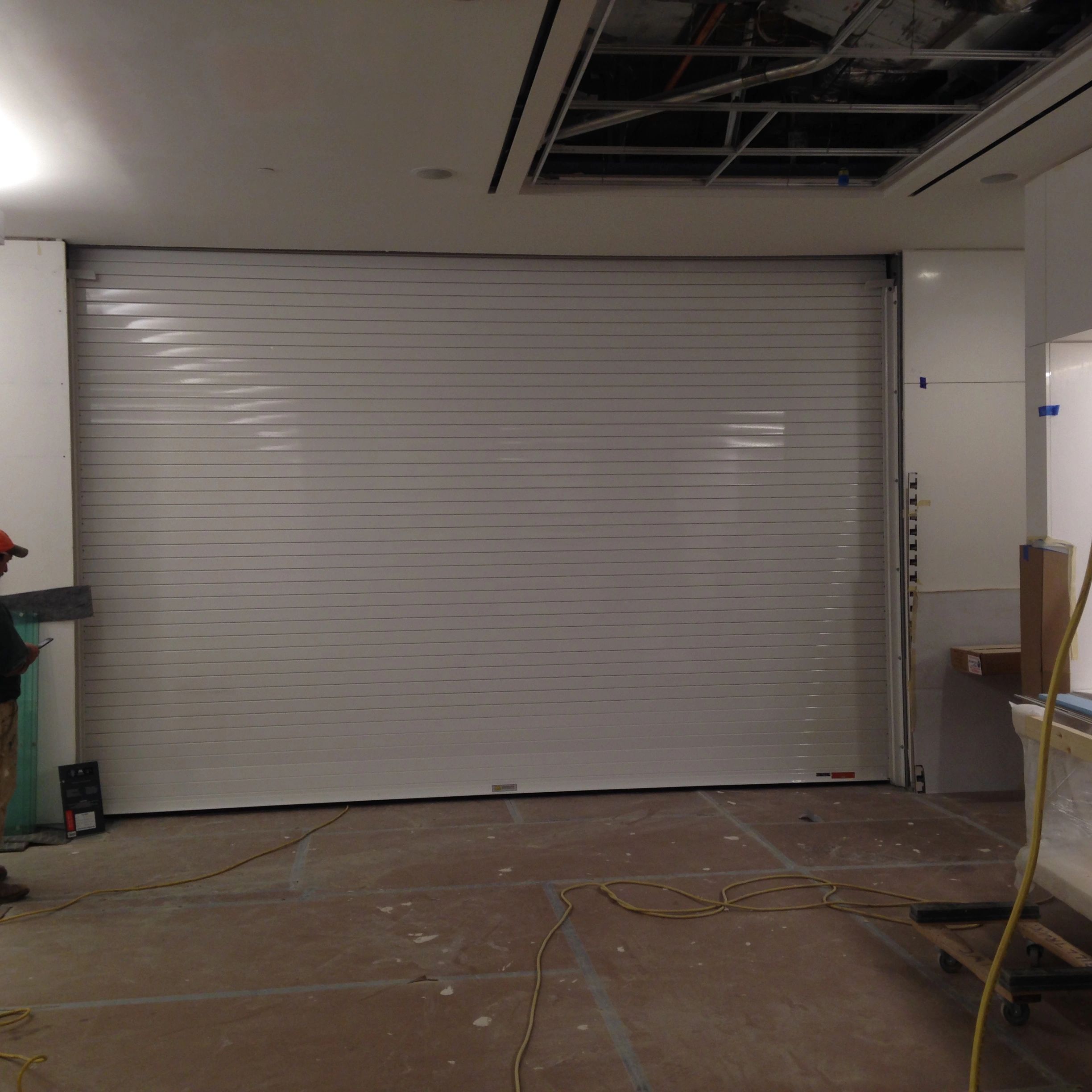 Indoor construction with a closed metal rolling door and exposed ceiling.