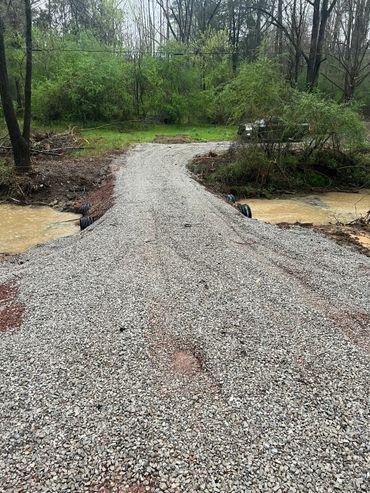 Newly constructed gravel driveway crossing a small creek in a wooded area.