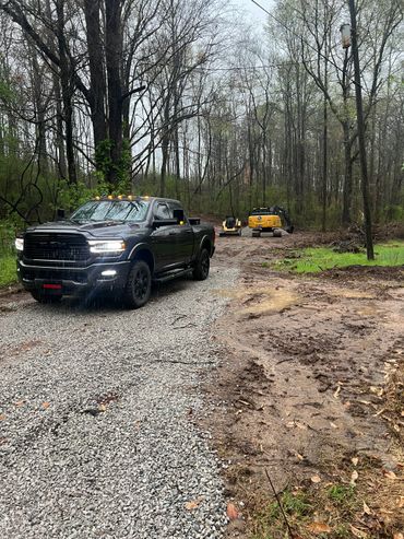 Black RAM truck parked on a gravel road with construction equipment in a wooded area.