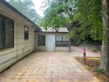 Backyard patio with tiled flooring and a small building with a white door.