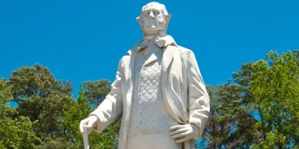 Statue of a man with a cane under a clear blue sky.