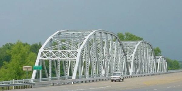 White metal arch bridge over a highway.