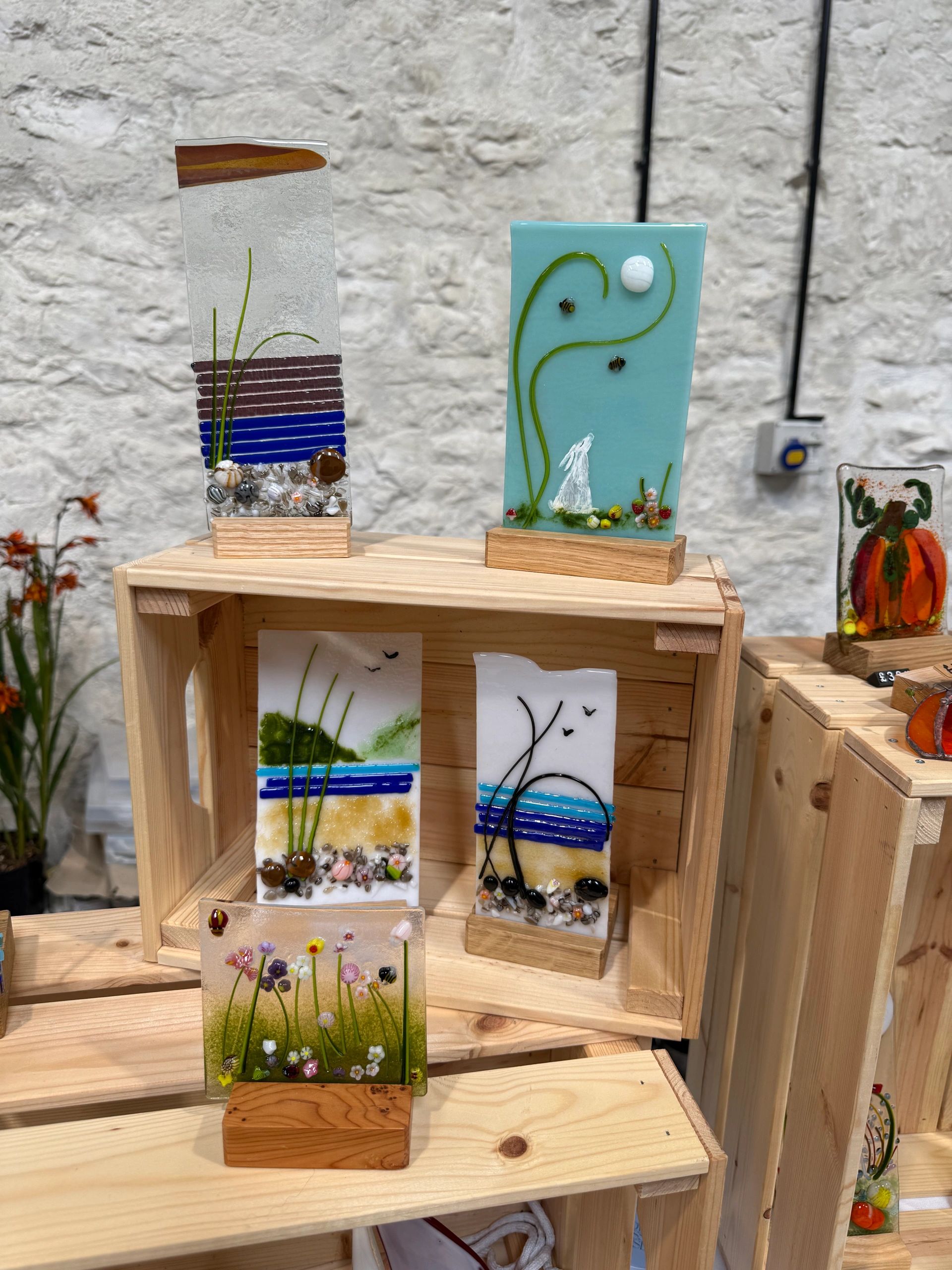 Decorative glass art pieces with nature-inspired designs on wooden stands.