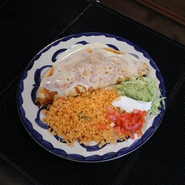 A plate of Mexican food with rice, a sauce-covered burrito, guacamole, sour cream, and diced tomatoes.