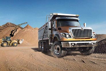 A truck at a construction site with sand piles and a crane in the background