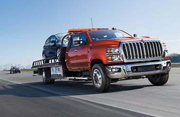 A red tow truck carrying a car driving along