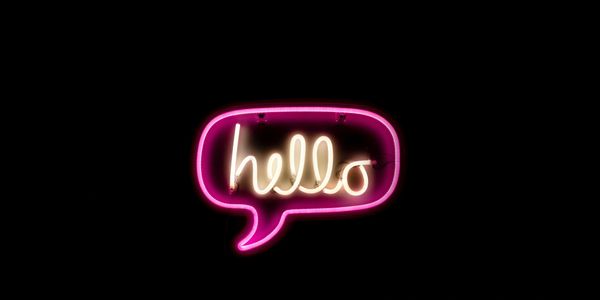 Neon sign with the word 'hello' in a speech bubble on black background.