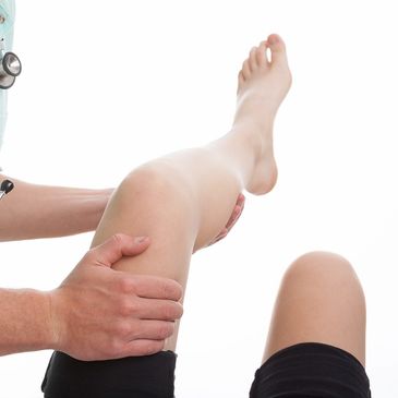 A chiropractor examines a patient's raised knee, possibly for injury, in a clinical setting.