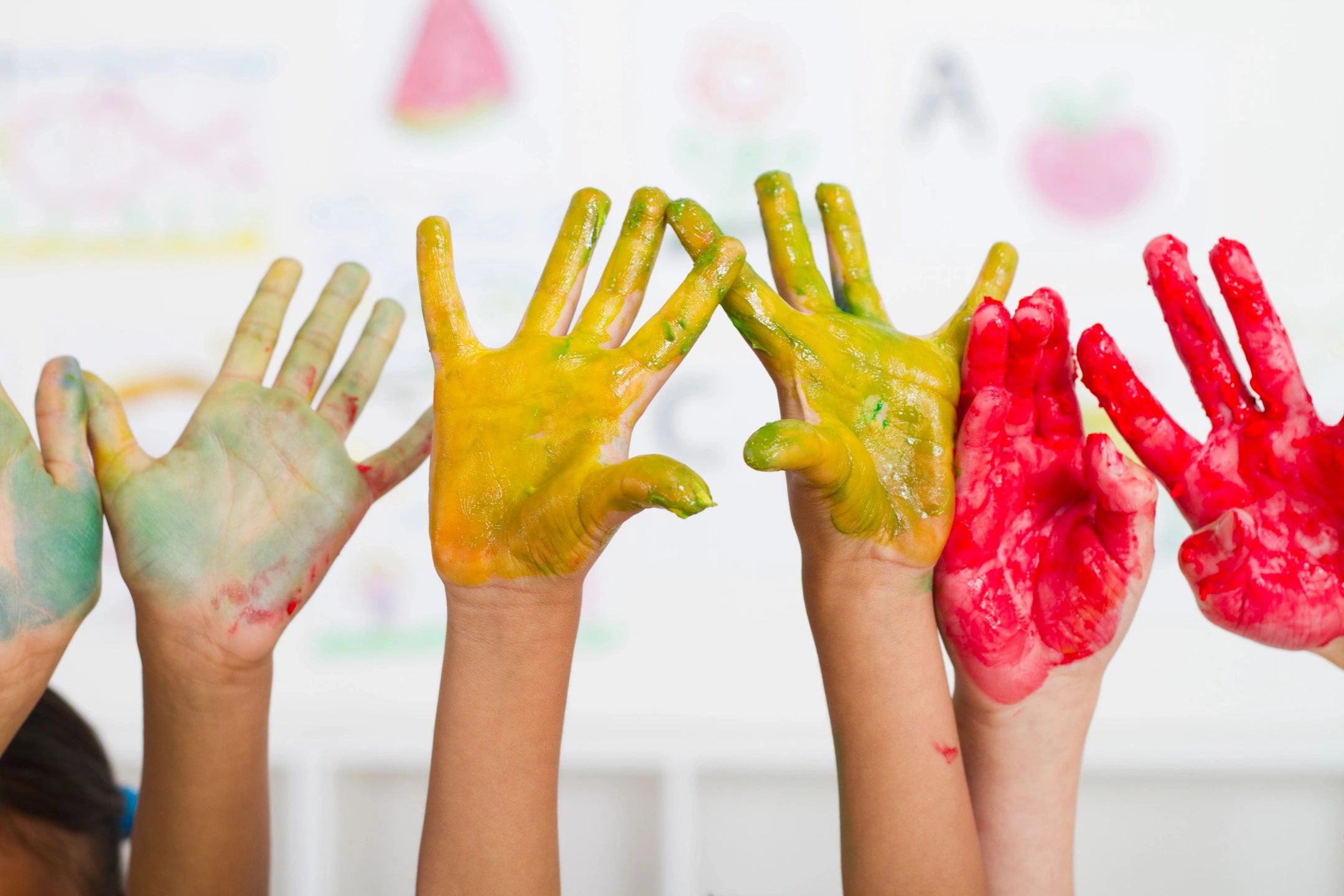 Small hands covered in bright paint held high in the air for the camera