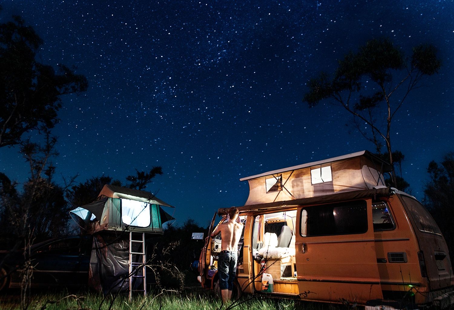 Two campervans parked under a starry night sky with trees in the background