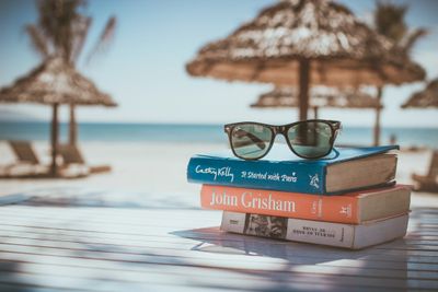 Color photo of beach with a stack of books and pair of sunglasses on a table in the foreground
