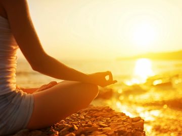 woman sitting wit legs folded in facing the sun and lake water while using good posture meditating