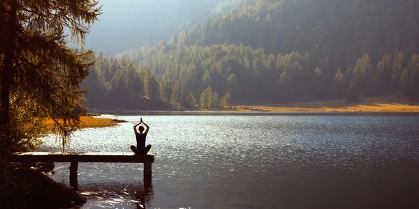 A person sitting on a pier doing yoga in the middle of nature surrounded by a lake