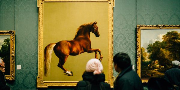 Two people looking at a framed painting of a horse